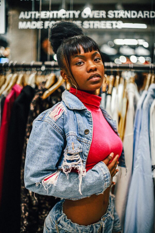 Stylish portrait of a Black woman in a denim jacket inside a clothing store.