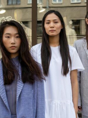 Three Asian women in fashionable clothing pose confidently in an urban outdoor setting, showcasing modern style.