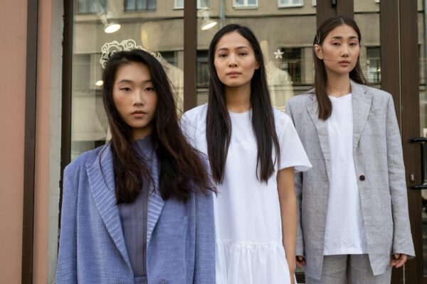 Three Asian women in fashionable clothing pose confidently in an urban outdoor setting, showcasing modern style.