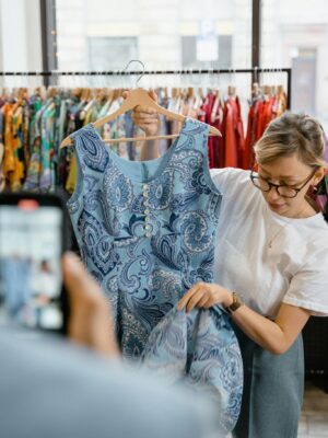 Woman inspecting a blue patterned dress in a retail clothing store. Fashion and shopping concept.